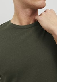 Olivenfarvet t-shirt med korte ærmer og rund halsudskæring, lavet af et glat, strækbart materiale. Har et tætsiddende design og en subtil ribbet tekstur.