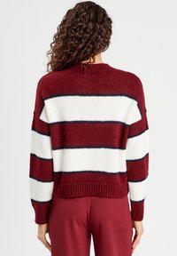 Pull en tricot avec des rayures bourgogne, blanches et marines. Manches mi-longues, bords côtes aux poignets et à l'ourlet, coupe décontractée, texture douce.