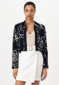 Κομμένο ναυτικό σακάκι με λευκό λουλουδάτο μοτίβο; σχέδιο με κουμπιά στην μπροστινή πλευρά, μυτερό γιακά και μακριά μανίκια. Συνδυασμένο με μπεζ μπλούζα και λευκή φούστα.