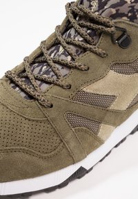 Sneakers w kolorze oliwkowym z cholewką z zamszu i siateczki, z wzorem w kamuflaż, teksturowanymi akcentami oraz czarną gumową podeszwą dla lepszej przyczepności.