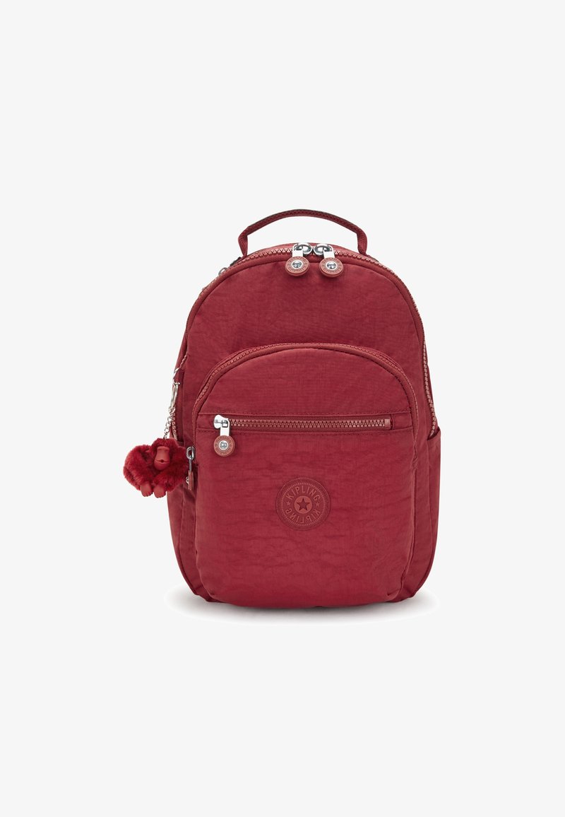 Sac à dos rouge compact avec poche avant zippée, poignée supérieure, fermeture double zip, et un petit porte-clés en peluche attaché sur le côté.
