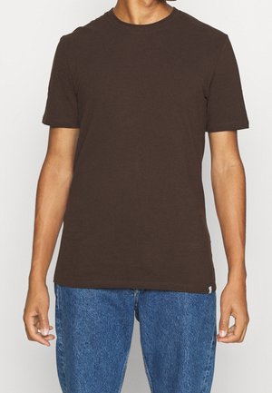 Mørkebrun bomulds T-shirt med korte ærmer og rund halsudskæring, parret med blå denim jeans. Enkel, ensfarvet design uden synlige mønstre.