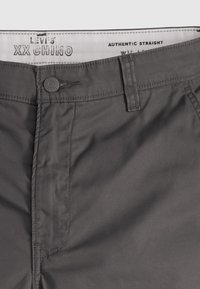 Pantaloni chino gri, fabricati dintr-un material din amestec de bumbac. Prezintă o croială dreaptă, închidere cu nasture și buzunare frontale cu cusături vizibile.