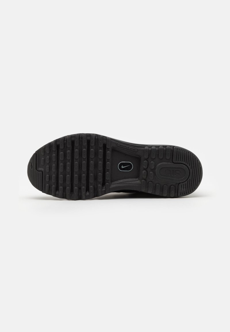 Suela de zapato deportivo negra con una superficie de goma texturizada, un patrón de banda de rodadura prominente y un pequeño detalle de logo.