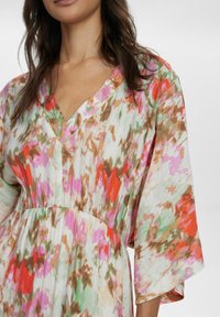 Rochie florală cu un amestec de nuanțe roz, portocaliu și verde, cu decolteu în V și mâneci largi, cu volane. Material texturat și talie strânsă.