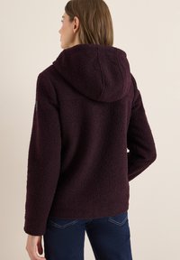Veste en polaire violet foncé avec une capuche, dotée d'un tissu texturé et d'une coupe décontractée. Design simple sans détails en métal visibles.