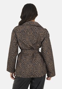 Brązowa i czarna kurtka w wzór lamparta, z paskiem w talii, szerokim kołnierzem i długimi rękawami, wykonana z teksturowanej tkaniny.