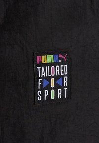 Logo Pumy z wielokolorowymi literami nad czarną łatą z napisem "DOPASOWANE DO SPORTU" z geometrycznymi kształtami na czarnym materiale.