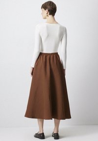Lange, bruine katoenen rok met een geraffineerde taille, een gladde textuur en een vloeiende silhouet, gecombineerd met een strakke, witte longsleeve top.