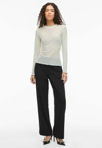 Długi, przezroczysty top w jasnoniebieskim kolorze z czarnymi groszkami, z falowanym dołem. Połączony z czarnymi szerokimi spodniami i butami na obcasie z zaostrzonym noskiem.