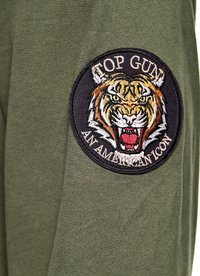 Oliven grøn beklædning med en broderet rund lap med et tigermotiv, ordene "TOP GUN" og "AN AMERICAN ICON" i sort og hvidt.