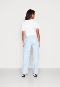 Camiseta branca combinada com calças claras de padrão azul. As calças apresentam um desenho xadrez e são usadas com ténis pretos e brancos.