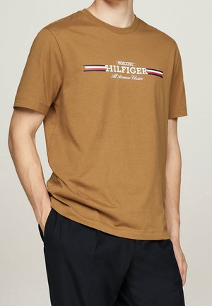 Brown cotton T-shirt featuring a crew neck and short sleeves, with a white and navy logo stripe across the chest.