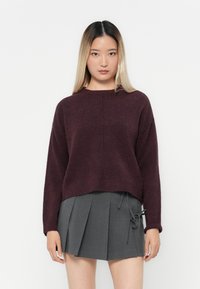 Burgundowy sweter z dzianiny o luźnym kroju i okrągłym dekolcie, zestawiony z szarym plisowanym spódnicą z wiązaniami po bokach.