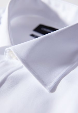 Hvid skjorte med klassisk krave, glat tekstur, en enkelt knap på kraven og en synlig mærkelabel i sort.