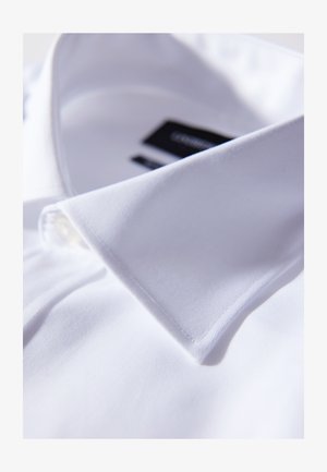 Valkoinen kauluspaita, jossa on klassinen kaulus, sileä rakenne, yksi nappi kauluksessa ja näkyvä musta brändilogo.