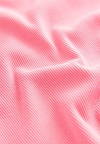 Ružová rebrovaná látka zobrazujúca jemné vertikálne čiary, s mäkkou textúrou a jemným leskom, vytvárajúca jemné vlny a záhyby.