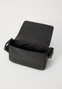 Black rectangular crossbody bag made of textured material, featuring a magnetic flap closure and adjustable strap; unlined interior.