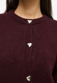 Bordeauxroter Strickcardigan mit rundem Halsausschnitt und silbernen herzförmigen Knöpfen auf der Vorderseite. Weiche Textur und klassischer Schnitt.