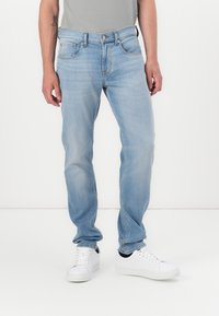 Light blue denim jeans with a straight cut, five-pocket design, and a front button closure, paired with white sneakers.