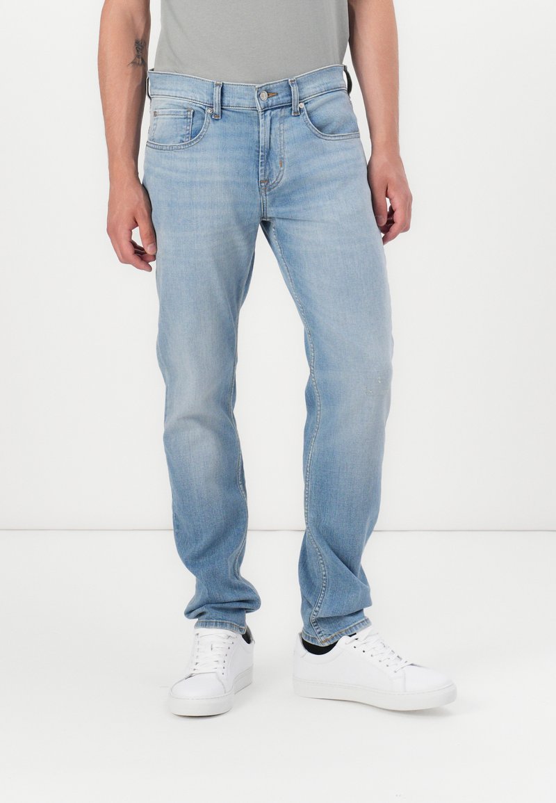 Light blue denim jeans with a straight cut, five-pocket design, and a front button closure, paired with white sneakers.