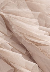 Warstwowy tiul w delikatnym beżu z złotymi metalicznymi kropkami, z falbaniastymi brzegami i lekką, przewiewną fakturą.