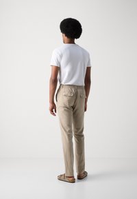 White short-sleeve t-shirt, beige elastic waist pants with back pockets, and brown slip-on sandals, viewed from the back.
