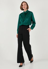 Green satin blouse with tie detail, paired with black elastic-waist wide-leg trousers and black high-heeled shoes. Smooth, glossy textures.
