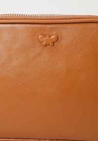 Borsa in pelle marrone con una texture liscia e un piccolo logo a farfalla in rilievo sulla parte anteriore. Cerniera metallica lungo il bordo superiore.