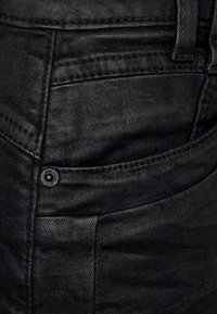 Mustat farkut, joissa on teksturoitu pinta, niitattu tasku ja tasaiset saumat. Kangas näyttää olevan hyvin valmistettua ja kestävää.