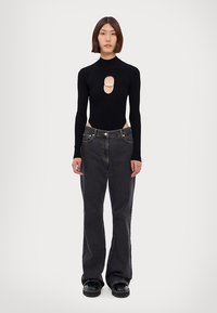 Schwarzer, gerippter Body mit einem frontalen Ausschnitt und Perlenakzent, kombiniert mit dunkelgrauen, weiten Jeans und klobigen, schwarzen Schuhen. Minimalistisches Design.