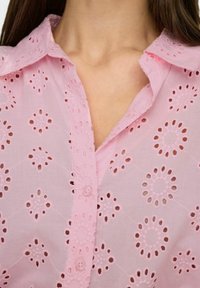 Blusa rosa chiaro con ricami floreali e lavorazione ad aria, colletto classico e chiusura con bottoni. Tessuto in cotone morbido.