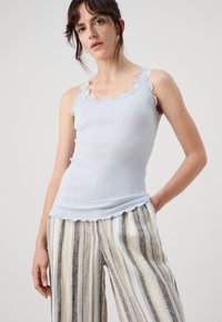 Lyseblå ribbet tanktopp med bølget blondekant. Har en tettsittende fasong og myk tekstur, kombinert med stripete, løstsittende bukser.