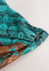 Tissu turquoise et marron avec des motifs cachemire complexes réunis à un poignet élastique noir avec un petit bouton noir.