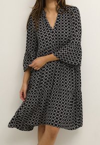 Vestido negro y blanco con estampado, escote en V, mangas acampanadas y falda de volantes. Tejido ligero con un diseño geométrico.