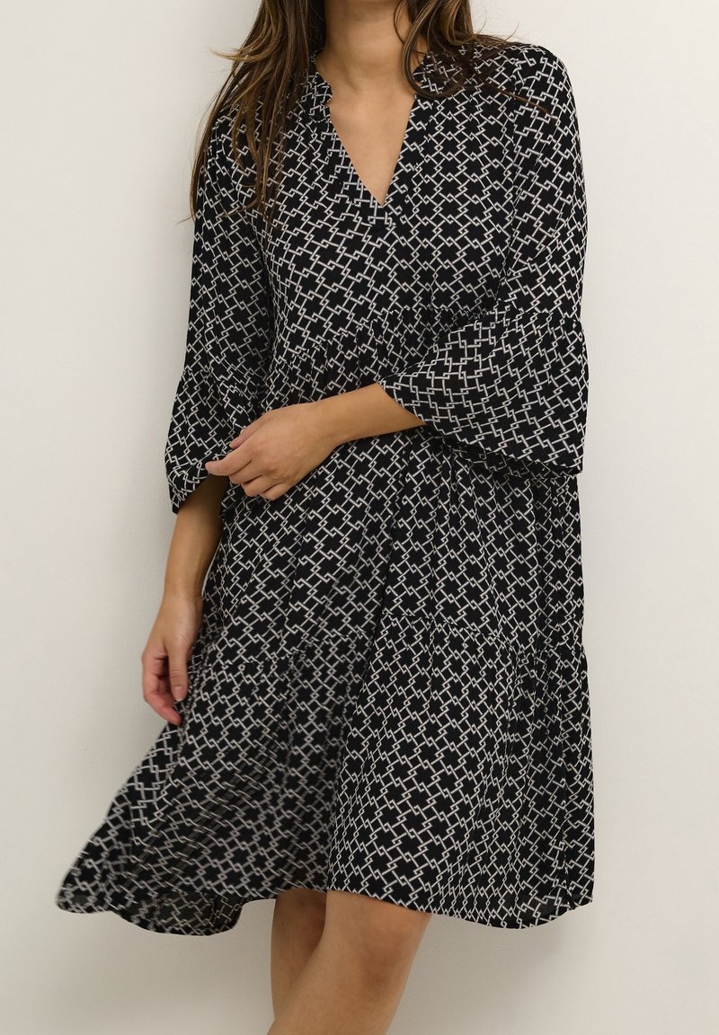 Vestido negro y blanco con estampado, escote en V, mangas acampanadas y falda de volantes. Tejido ligero con un diseño geométrico.