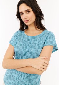 Mėlynos spalvos trumpų rankovių palaidinė, turinti tekstūruotą taškų ir linijų raštą, apvalų iškirpimą ir švelnią medžiagą.