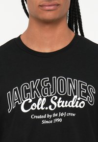 T-shirt de algodão preto com texto impresso em branco em destaque: "JACK&JONES Coll.Studio" e "Criado pela equipa J&J Desde 1990." Design clássico com decote redondo.