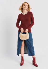 Burgundijas vilnas džemperis ar garām piedurknēm un rotātiem dekoltē, apvienots ar džinsa maksi svārkiem ar priekšu izgriezumu. Sarkanās papēžu zābaki un pūkains bēšs rokassomas.