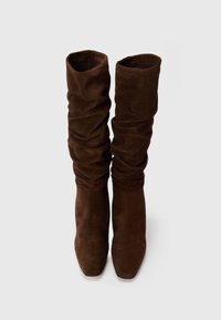 Brown suede knee-high boots with a slouchy design and square toes, featuring a smooth texture and a soft finish.