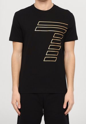T-shirt in cotone nero con una grande grafica diagonale a strisce dorate a forma di '7' sul davanti. Girocollo e maniche corte. Vestibilità casual.