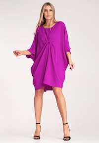 Fuksjowa sukienka luźnego kroju z okrągłym dekoltem, krótkimi rękawami i węzłem z przodu. Gładka tekstura, do kolan z asymetrycznym dołem.