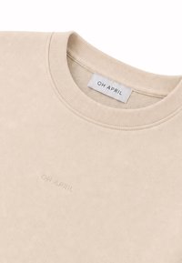 Sweat-shirt beige à col rond avec col côtelé et texte en relief "OH APRIL" sur la poitrine, avec une étiquette de marque à l’intérieur de l’encolure.