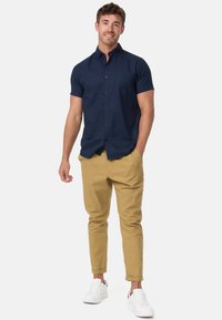 Camisa de botón de manga corta en azul marino, pantalones tapered color beige y zapatillas blancas. La tela parece suave con un diseño de cuello clásico.