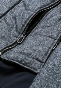 Gray, textured jacket featuring black zippers, a quilted design, and a smooth interior lining. Notable details include branded zipper pull.