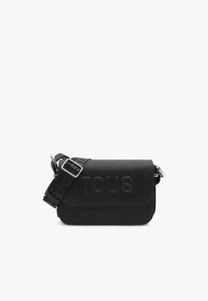 Sac bandoulière noir en matériau synthétique texturé. Il présente un logo "TOUS" gaufré, une sangle réglable avec marquage et du matériel en argent.