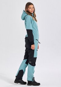 A teal and black insulated one-piece suit with a hood, featuring a zippered front, side pockets, and adjustable cuffs. Textured waterproof material.