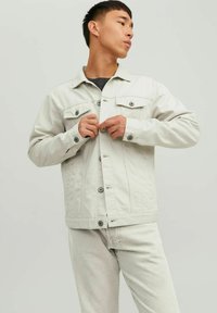 Giacca di jeans grigio chiaro con chiusura a bottoni, due tasche sul petto e colletto classico. Presenta una vestibilità leggermente attillata e cuciture robuste.