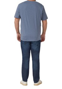 Niebieski bawełniany t-shirt z okrągłym dekoltem i krótkimi rękawami, noszony z ciemnymi jeansami i białymi butami, widziany od tyłu.