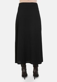 Jupe maxi noire en tissu lisse et fluide, avec une taille haute. Assortie à des bottes à talons, brunes, arrivant au genou.